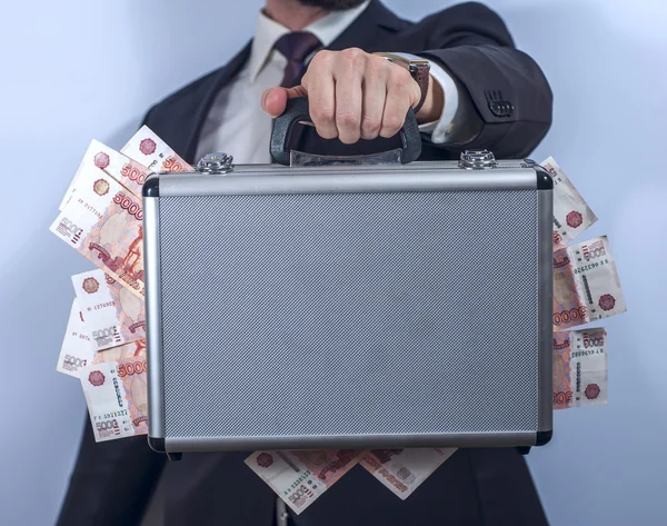 Man in suit holds metal briefcase full of money