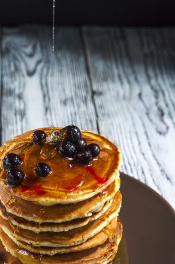 Siyah frenk üzümü ve rustik arka plan üzerinde kahverengi tabakta bal ile ev yapımı krep yığını