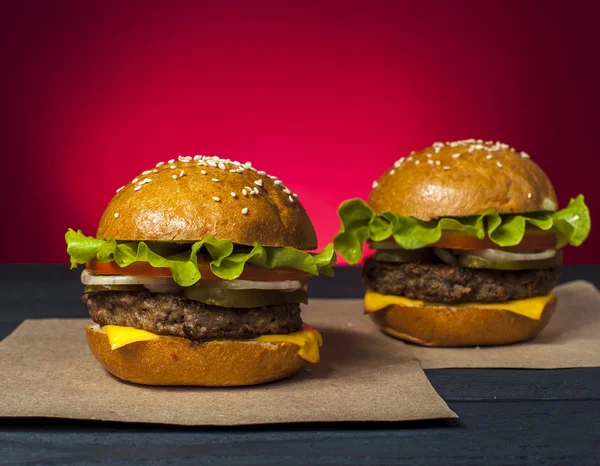 Ahşap masa üzerinde sebze ile iki iştah açıcı hamburger. Fast food, abur cubur. Sağlıksız yiyecek konsepti.