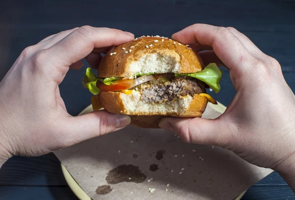 Appetizing hamburger with vegetables on white plate with fork and knife on wooden table. Fast food, junk food. Hamburger in woman's hands. Unhealthy food concept. — Φωτογραφία Αρχείου