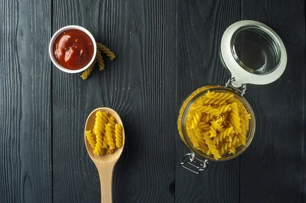 Makaron fusilli w słoiku, szklanka sosu pomidorowego i łyżka na drewniane tła. Dania kuchni włoskiej. — Zdjęcie stockowe