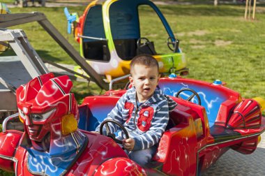 Boy driving car toy in the amusement park clipart
