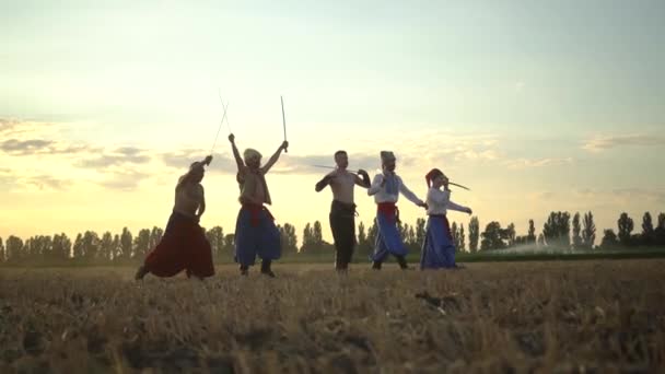 Gruppe von Kosakenmännern in traditioneller Kleidung schwingt und dreht scharfe Schaschkas gegen den bewölkten Himmel bei Sonnenuntergang — Stockvideo