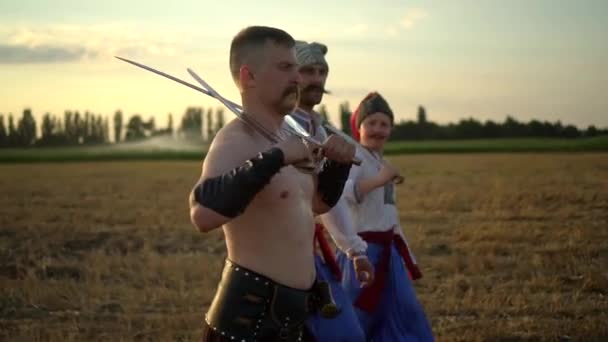 Gruppo di uomini cosacco in abiti tradizionali oscillazione e filatura shashka taglienti contro cielo nuvoloso tramonto — Video Stock