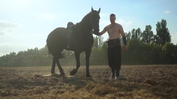 En man går med en häst på fältet — Stockvideo
