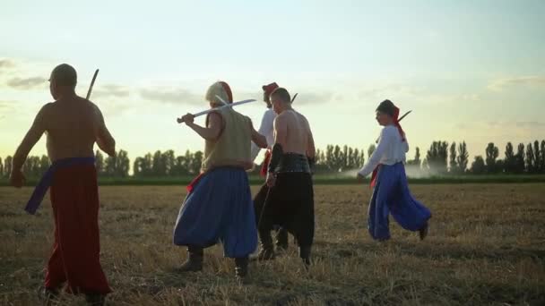 Grupo de hombres cosacos en ropa tradicional balanceándose y girando shashkas afilados contra el cielo nublado puesta de sol — Vídeos de Stock