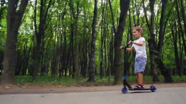 Chlapec jezdí na skútru v městském parku — Stock video