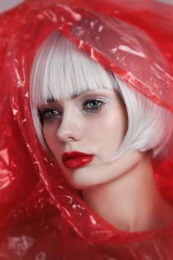 Platin sarısı saçlı, kırmızı plastik yağmurluk giyen güzel bir kadının klasik portresi.