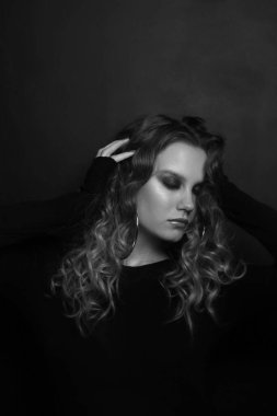 Uzun kıvırcık saçlı ve dumanlı göz makyajlı güzel bir kızın klasik siyah beyaz portresi.