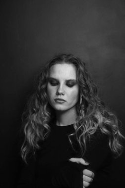 Uzun kıvırcık saçlı ve dumanlı göz makyajlı güzel bir kızın klasik siyah beyaz portresi.