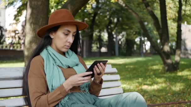 Bliskowschodnia kobieta czyta e-booki siedząc na ławce w parku. Używając komputera z tabletką. Student dziewczyna czyta e-book — Wideo stockowe