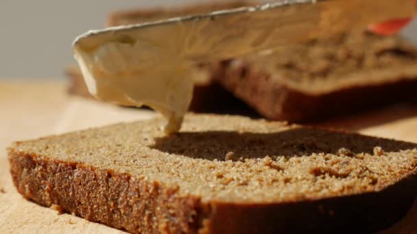 Espalhando manteiga vegan no pão de centeio sem laticínios e ovos. Faca manchando manteiga macia em fatia de pão ao nascer do sol da manhã. Close-up — Vídeo de Stock