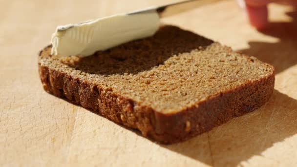 Menaburkan mentega vegan pada roti gandum tanpa susu dan telur. Pisau mengolesi mentega lembut di atas sepotong roti saat matahari terbit. Close-up — Stok Video