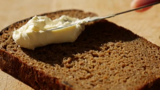 Ohne Milchprodukte und Eier vegane Butter auf Roggenbrot streichen. Messer schmiert weiche Butter auf Scheiben Brot am Morgen Sonnenaufgang. Nahaufnahme — Stockvideo