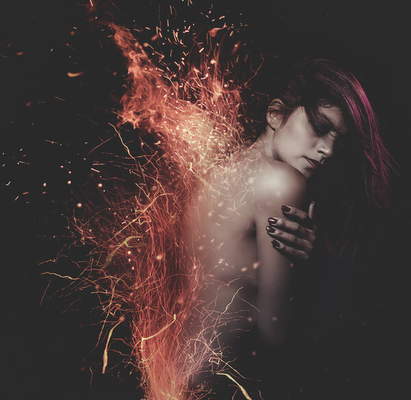 Young, beautiful, naked woman surrounded with sparks on black background