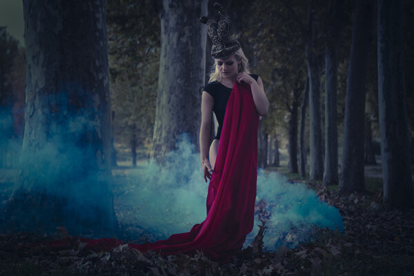 Forest romantic scene, beautiful blonde, fallen angel in black dress standing in the forest