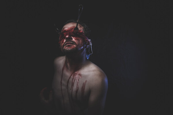 Naked man with blindfold soaked in blood