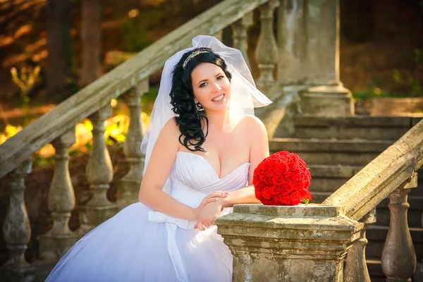 Hermosa novia se sienta en las escaleras de la antigua iglesia — Foto de Stock