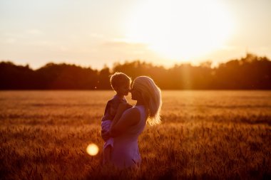 Anne ve oğlu gölün alan açık havada doğanın keyfini eğleniyor. Siluetleri güneşli gökyüzü üzerinde. Sıcak filtre ve film etkisi