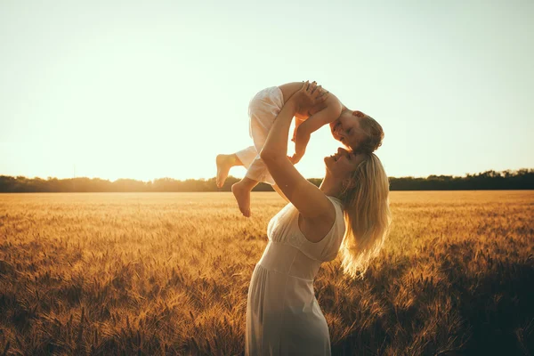 Mamá e hijo divirtiéndose junto al lago, campo al aire libre disfrutando de la naturaleza. Siluetas en el cielo soleado. Filtro caliente y efecto de película — Foto de Stock