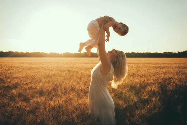 Mamá e hijo divirtiéndose junto al lago, campo al aire libre disfrutando de la naturaleza. Siluetas en el cielo soleado. Filtro caliente y efecto de película —  Fotos de Stock