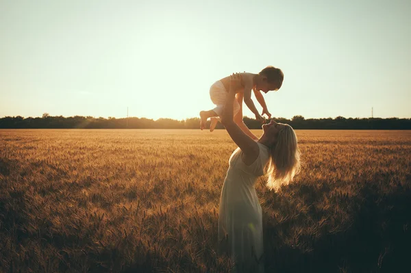 Mãe e filho se divertindo junto ao lago, campo ao ar livre apreciando a natureza. Silhuetas no céu ensolarado. Filtro quente e efeito filme — Fotografia de Stock