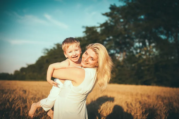 Mamá e hijo divirtiéndose junto al lago, campo al aire libre disfrutando de la naturaleza. Siluetas en el cielo soleado. Filtro caliente y efecto de película — Foto de Stock