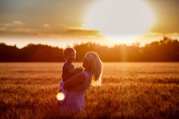 Mamá e hijo divirtiéndose junto al lago, campo al aire libre disfrutando de la naturaleza. Siluetas en el cielo soleado. Filtro caliente y efecto de película —  Fotos de Stock