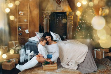 Güzel kahverengi saçlı anne ve sevimli oğlan yerde oturuyor ve Noel ağacının arka planındaki bir kutuda hediyeleri açıyor..