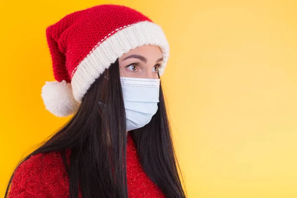 Fiatal nő orvosi maszkkal és télapó sapkával fehér háttéren. Karácsony a karanténban. — Stock Fotó