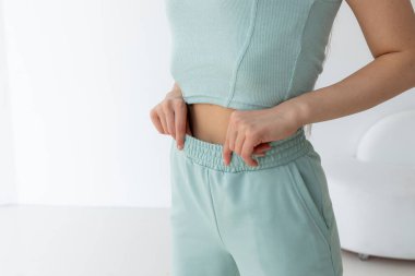 İnce belini ölçen ince bir kadın. Yeşil spor giyimli. beyaz arkaplanda