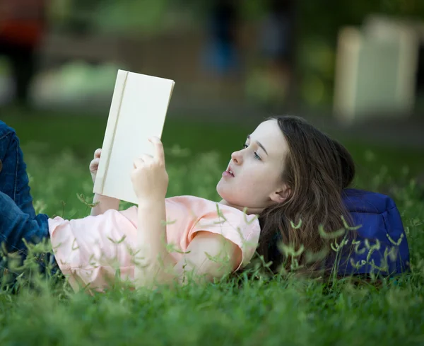 女孩躺在户外阅读本书的草地上 — 图库照片