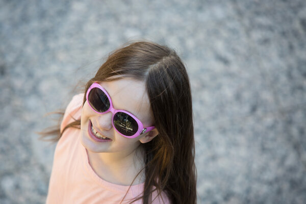 Happy attractive girl with fun pink sunglasses looks up at the c