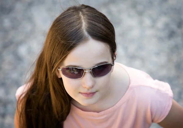 Flicka med solglasögon ser upp mot en grå trottoar Stockbild