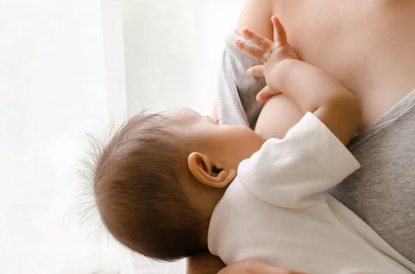 Mãe amamentando seu bebê recém-nascido ao lado da janela — Fotografia de Stock