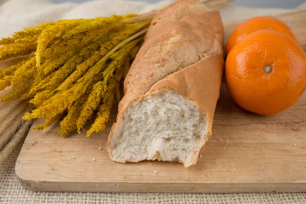 Baguettes de pan francés sobre tabla de pan y naranjas de mandarina — Foto de Stock