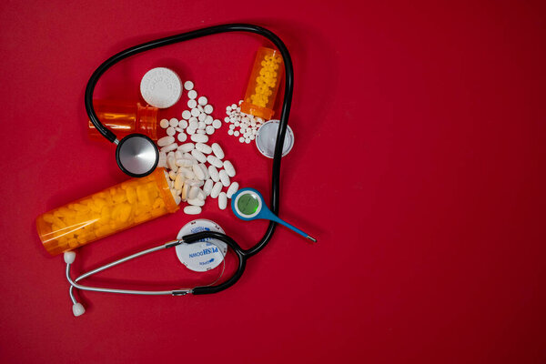 Three RX containers spilled out on a table top surrounded by a black Stethoscope and Thermometer. 
