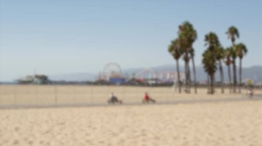 Kaliforniya plaj estetiği, insanlar bisiklet yolunda bisiklet sürüyor. Bulanık, odaklanmış arka plan. Santa Monica Amerikan Pasifik Okyanusu Tatil Köyü, Los Angeles CA ABD 'deki iskele ve palmiyelerdeki eğlence parkı.