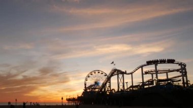 Klasik dönme dolap, Santa Monica Pasifik Okyanusu Sahili 'ndeki iskeledeki lunapark. Kaliforniya 'nın yaz zamanı estetik, ikonik manzara, Los Angeles' ın sembolü, CA USA. Günbatımı altın gökyüzü ve eğlence