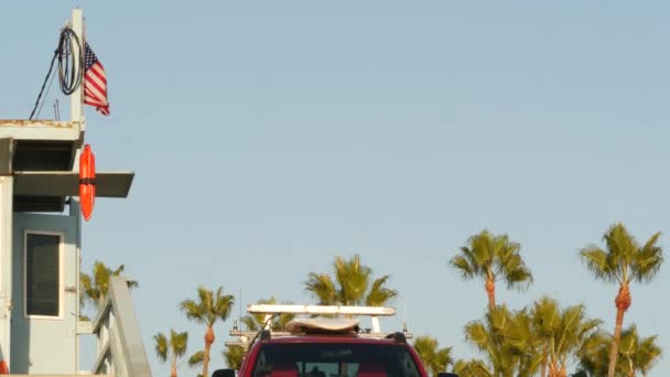 İkonik retro ahşap cankurtaran kulesi ve Sahil Güvenlik kırmızı arabası. Can simidi, Amerikan bayrağı ve mavi gökyüzüne karşı palmiye ağaçları. Yaz Kaliforniya estetiği, Santa Monica plajı, Los Angeles, CA USA — Stok video