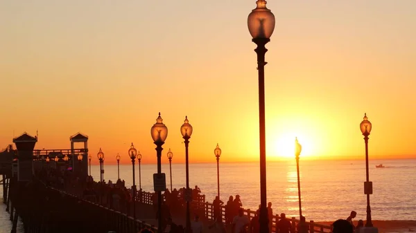 カリフォルニア州オーシャンサイド2019年11月17日 木製の桟橋と人々が歩く ウォーターフロントリゾート ロサンゼルス近くの夏休みを散歩観光客 日没の海のビーチ 熱帯の晴れオレンジの空 — ストック写真