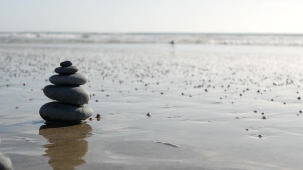 Rovnováha skal na mořském pobřeží, kameny u vln mořské vody. Pyramida z oblázků na písčitém břehu