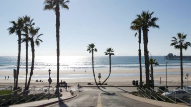 İnsanlar rıhtımda yürüyor, tropikal okyanus sahillerinde palmiye ağaçları ile. Oceanside, Kaliforniya ABD