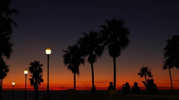 Palmer silhuett skymning himmel. Folk går. Oceanside pir, Kalifornien USA. Tropisk solnedgång vid stranden — Stockfoto