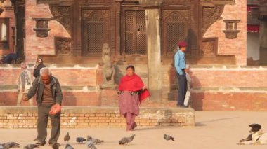 BHAKTAPUR, KATHMANDU, NEPAL - 18 Ekim 2018 Kraliyet Meydanı 'nda güvercinleri besleyen adam. Olgun bir adam antik kentteki Durbar meydanında kuşları besliyor. Günlük hayat, depremden sonra eski doğu şehri.
