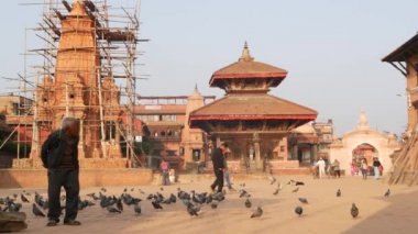 BHAKTAPUR, KATHMANDU, NEPAL - 18 Ekim 2018 Kraliyet Meydanı 'nda güvercinleri besleyen adam. Olgun bir adam antik kentteki Durbar meydanında kuşları besliyor. Günlük hayat, depremden sonra eski doğu şehri.
