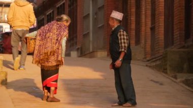 BHAKTAPUR, KATHMANDU, NEPAL - 18 Ekim 2018 Asyalı erkek ve yaşlı kadın ulusal kıyafetler içinde mutlu bir şekilde gülümsüyor, alıyor. Vatandaşlar günlük yaşam, depremden sonra antik doğu şehri..