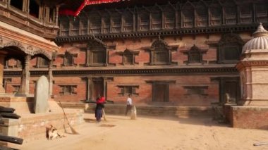 BHAKTAPUR, KATHMANDU, NEPAL - 18 Ekim 2018 Tapınak merdivenlerini süpüren yaşlı kadın. Hindu tapınağının merdivenlerini silip süpüren renkli kumaşlı yaşlı kadın. Durbar kraliyet sarayı
