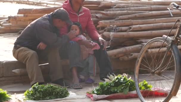 Bhaktapur Nepal October 2018路上で子供と一緒に座っている間 男性は喫煙します 近くの赤ちゃんと一緒に路上に座っている男性地元の市場で商品を販売しながら — ストック動画