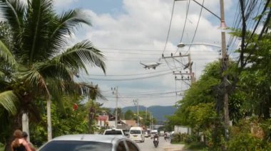 KOH SAMUI ADASI, THAILAND - 23 Haziran 2019 Tropikal kasabanın ana caddesine inen uçak. Bangkok havaalanına giden uçaklar, egzotik turistik tatil beldeleri. Motosikletli Taylandlılar